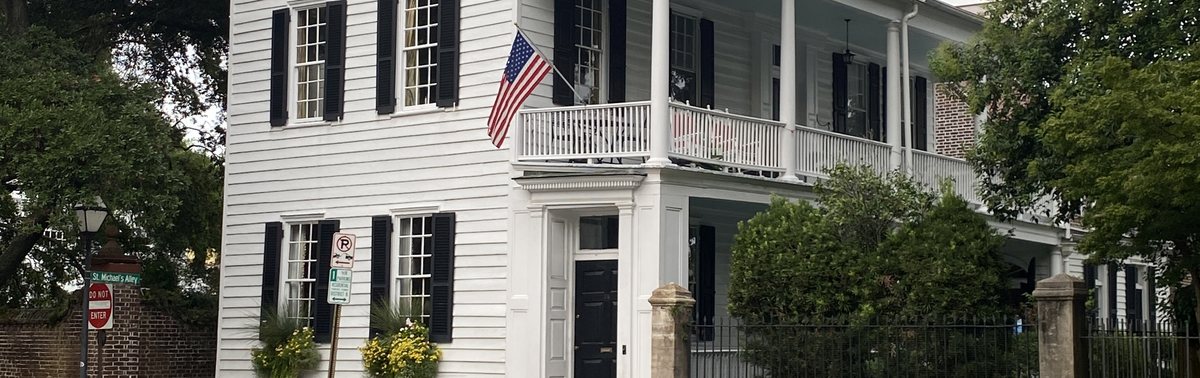 A white three-story Charleston single house with black shutters and a piazza on Meeting Street in Charleston SC